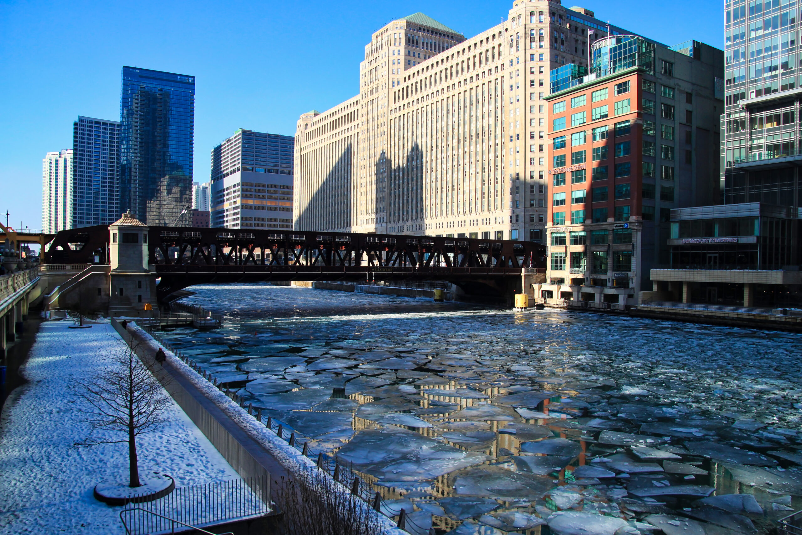The Chicago Riverwalk covered in deep snow with icy water and city bridges.