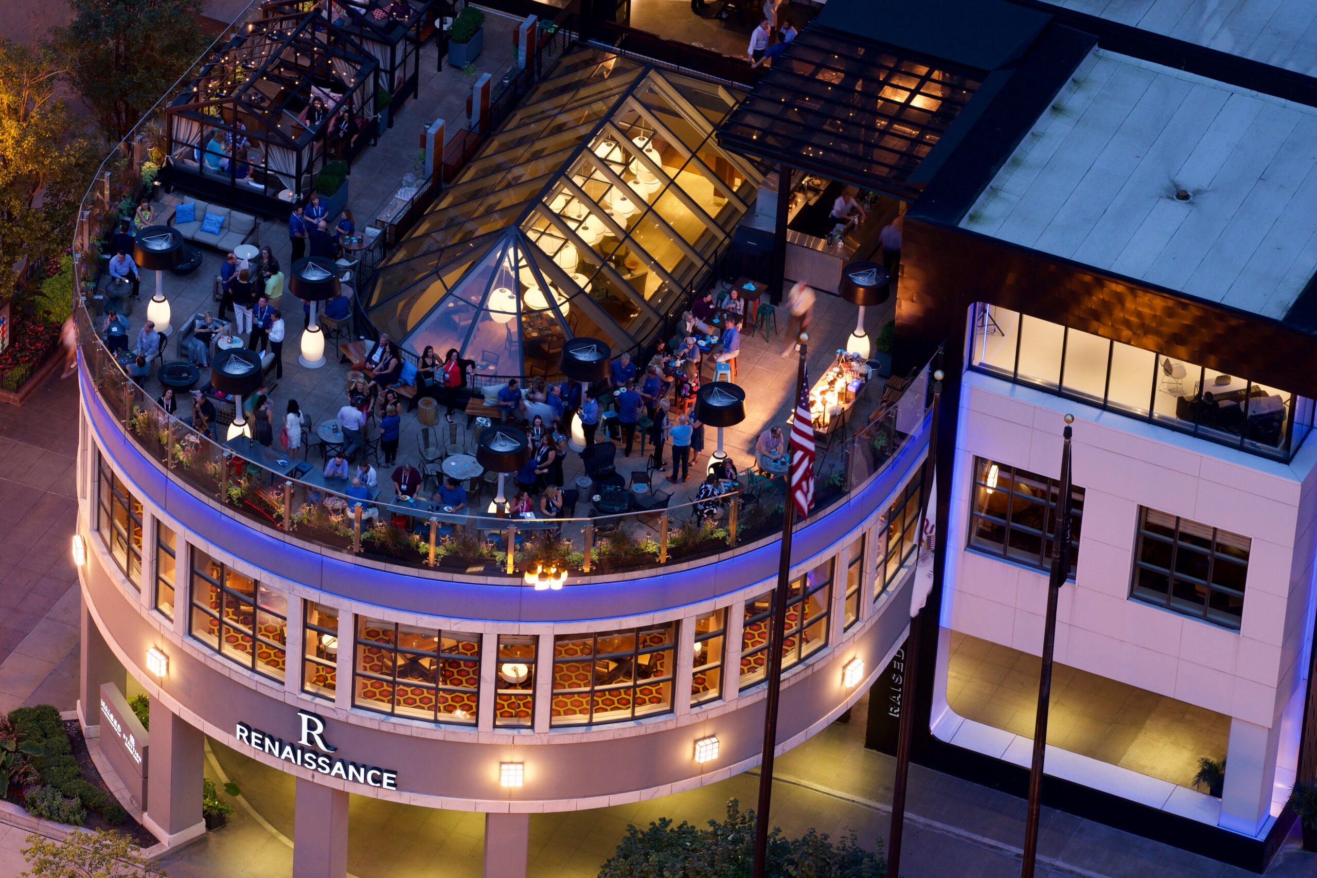 A lively rooftop bar in downtown Chicago filled with guests enjoying drinks and city views at dusk from a modern open-air terrace above the Renaissance hotel.
