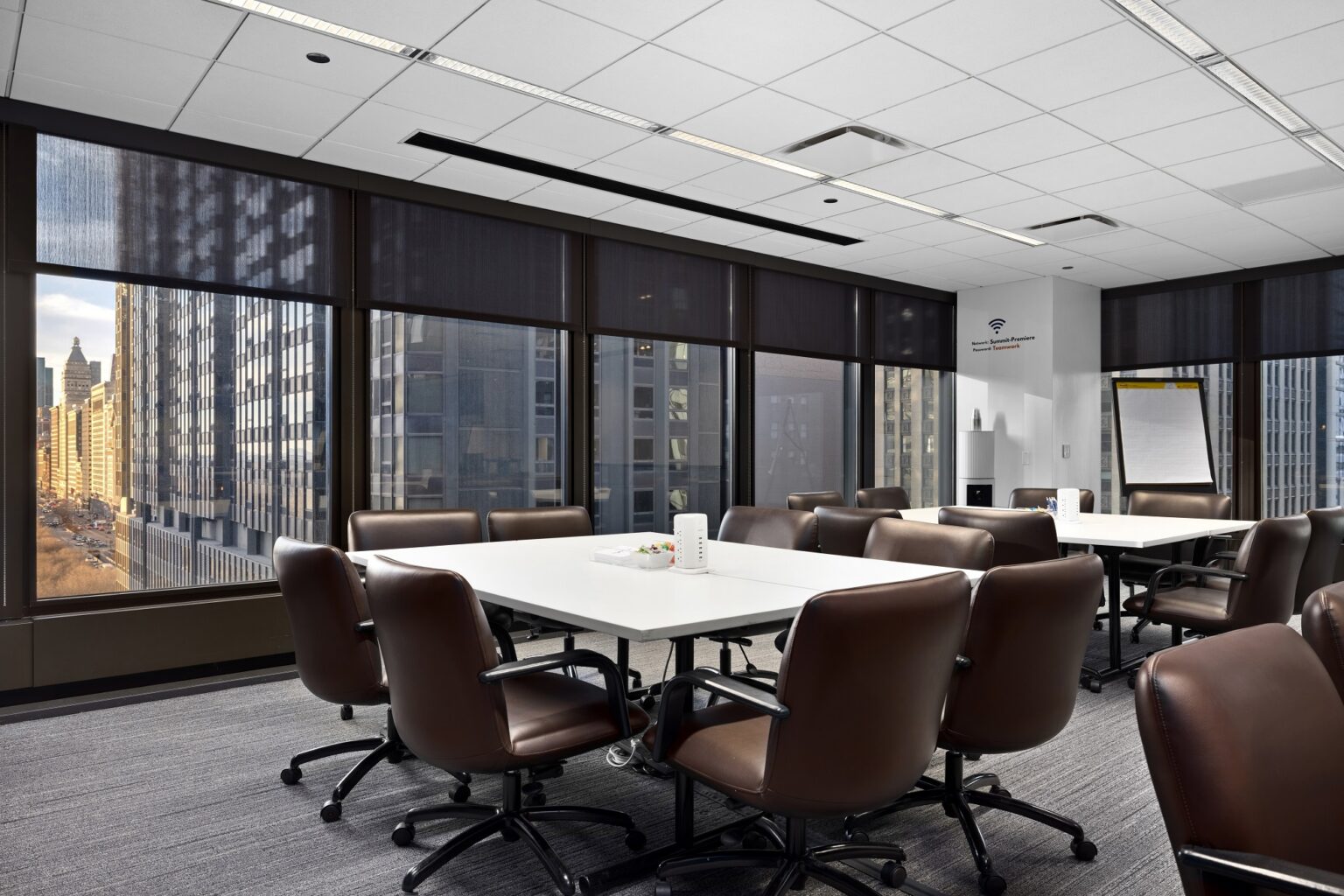 Meeting room at Summit Chicago with leather conference chairs, white tables, a flip chart, and floor-to-ceiling windows overlooking the downtown Chicago skyline.