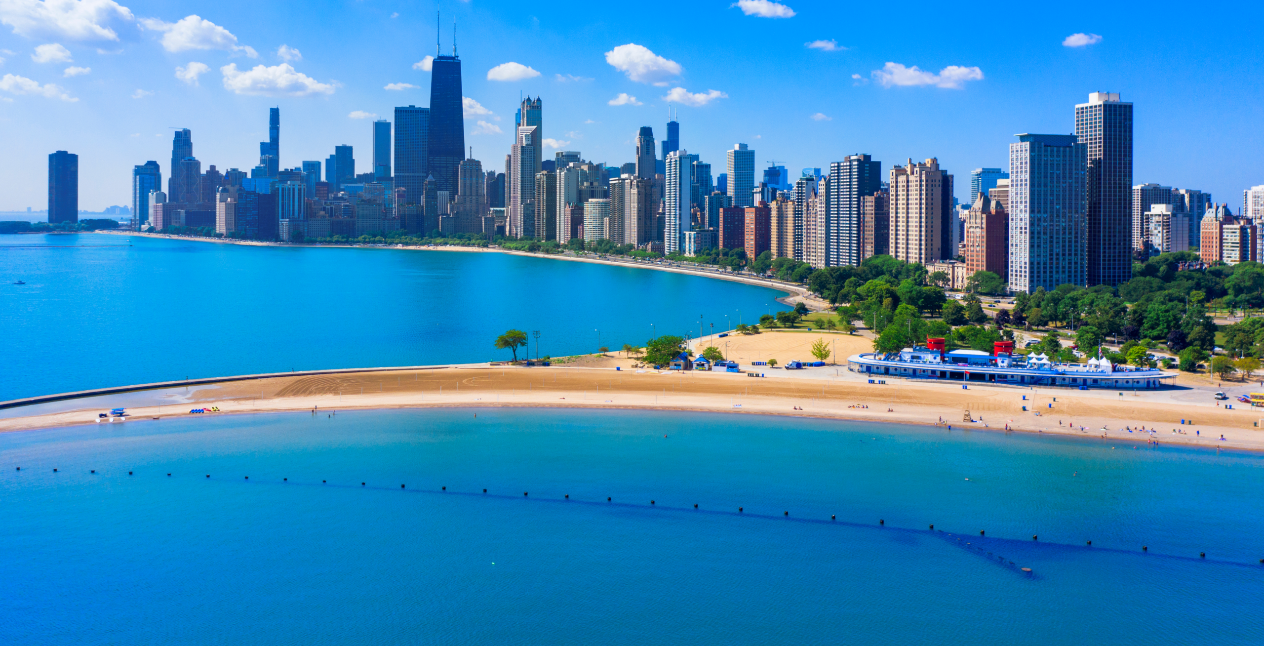 A panoramic view of North Avenue Beach along Lake Michigan, with Chicago’s skyline rising behind the sandy shoreline on a sunny day.