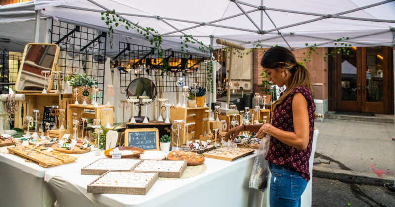 A person browses handmade jewelry at an outdoor vendor booth beneath a white canopy during a street fair in Midtown Manhattan.