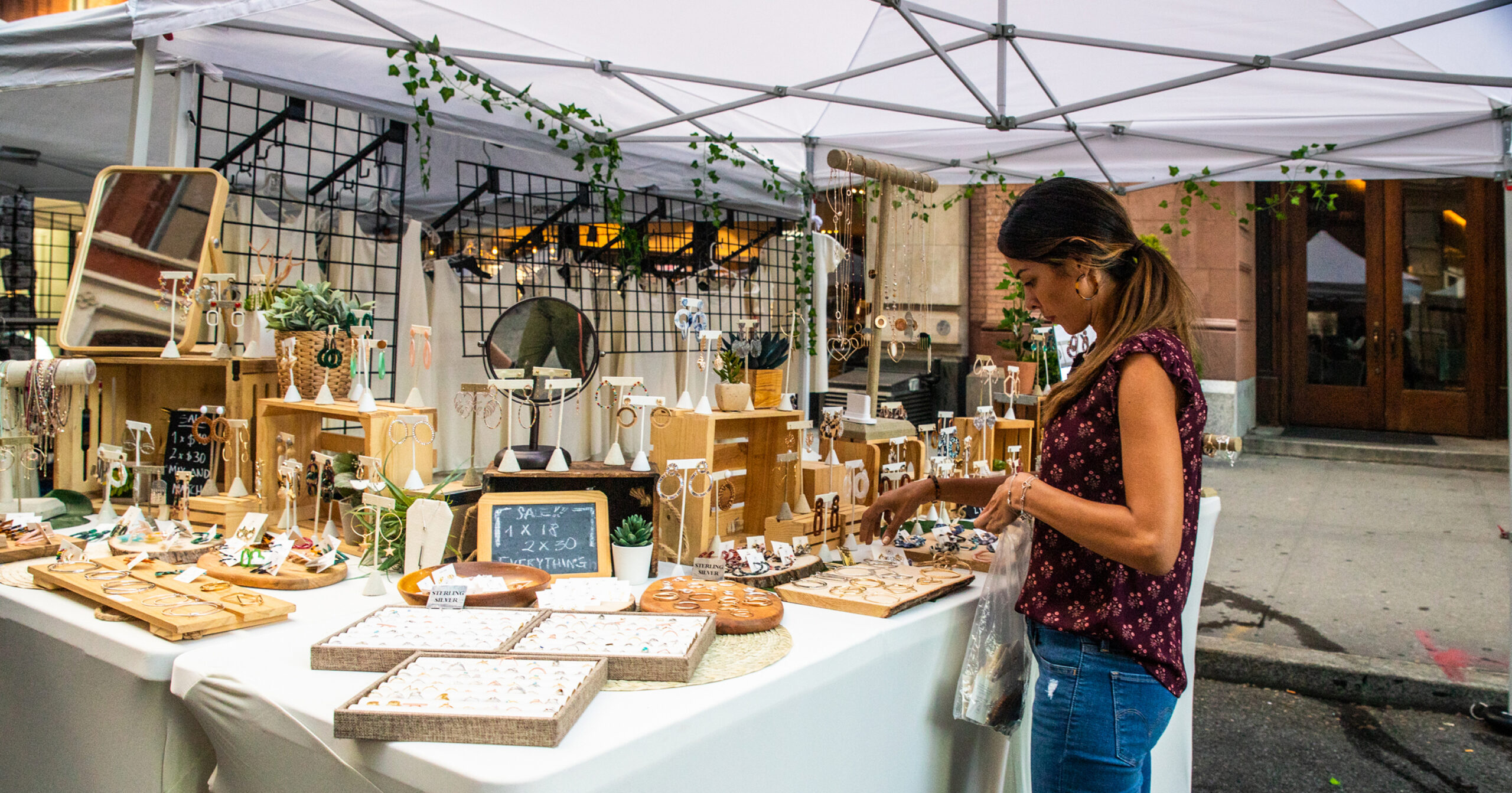 A person browses handmade jewelry at an outdoor vendor booth beneath a white canopy during a street fair in Midtown Manhattan.