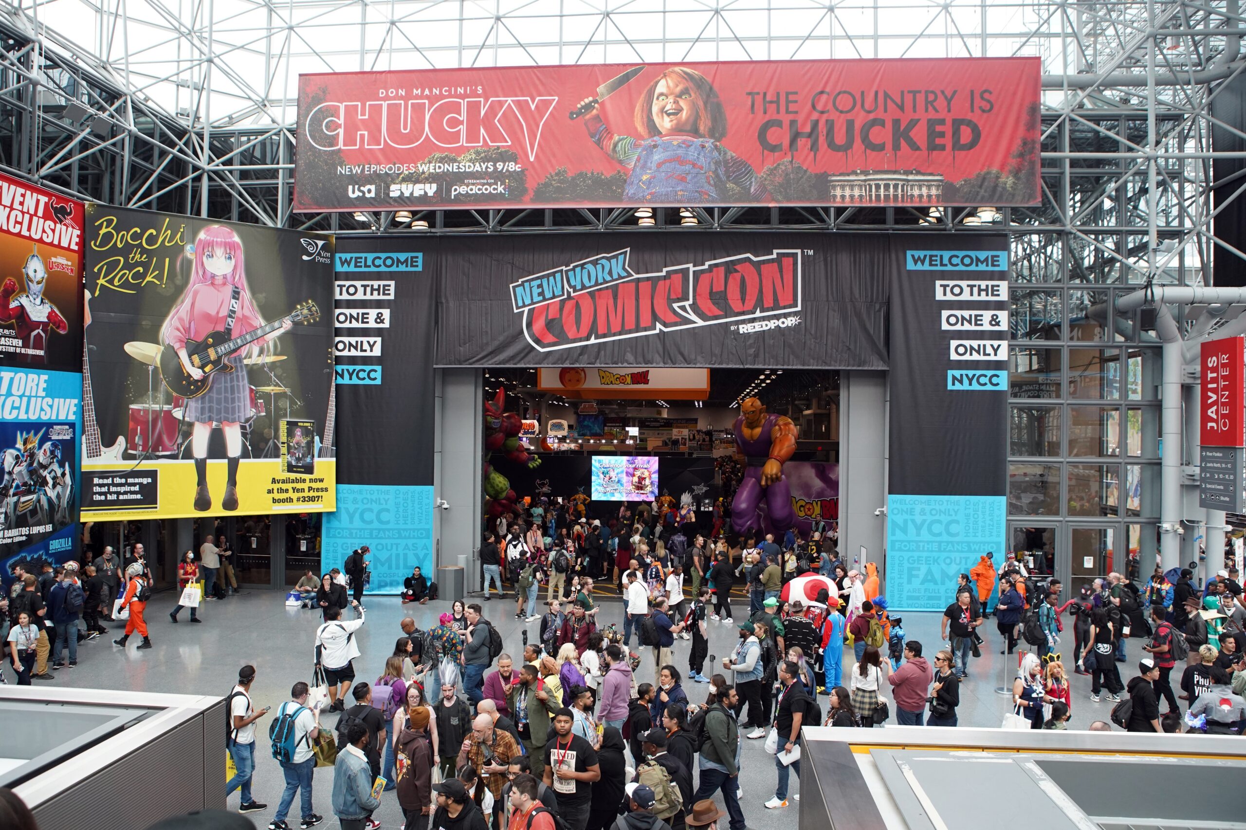 Crowds of fans gather at the entrance to New York Comic Con at the Javits Center, surrounded by Comic Con banners, character displays, and event signage.