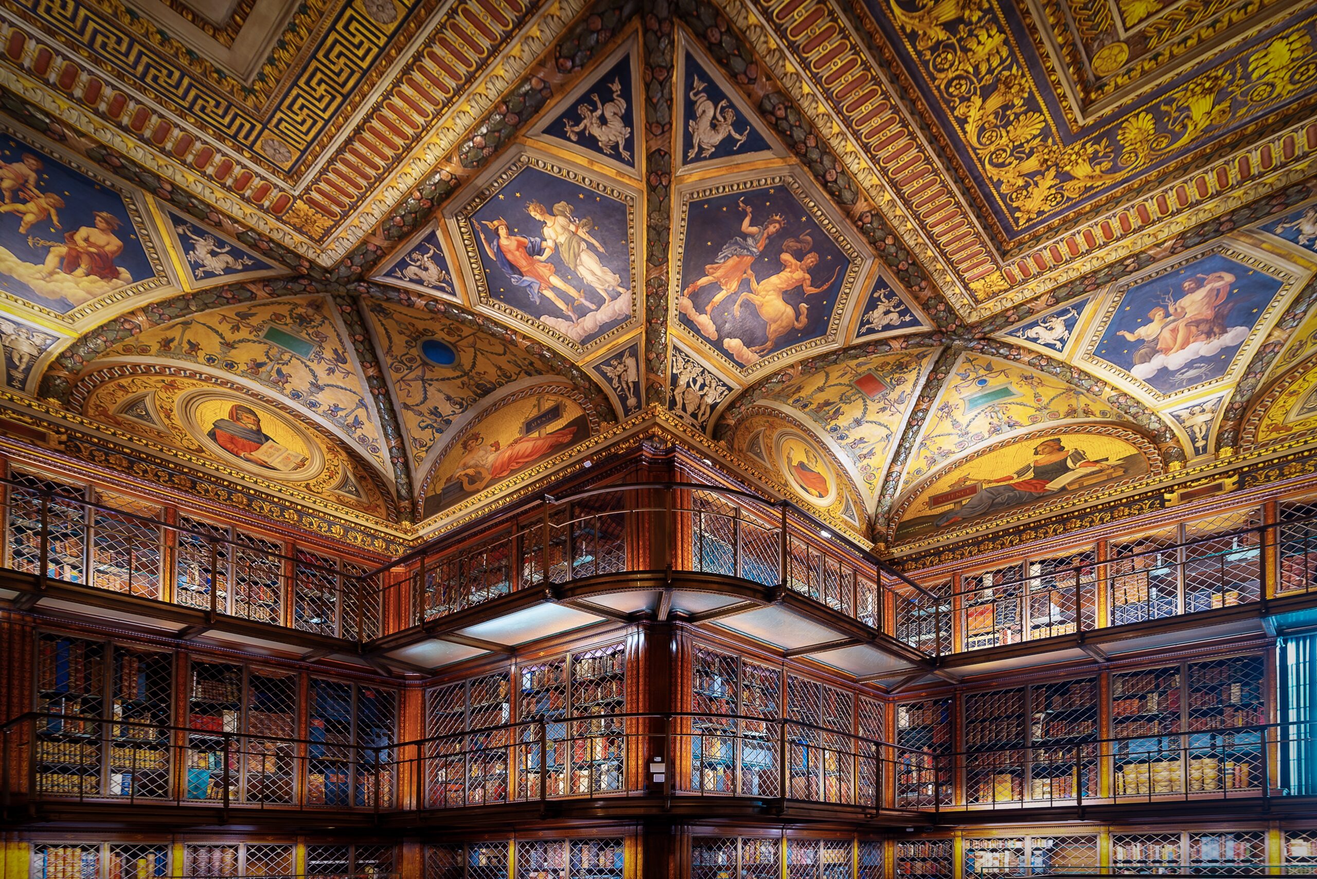 Ornate library with multi-level wooden bookshelves and a grand vaulted ceiling featuring gold detailing and Renaissance-style frescoes, things to do in nyc.