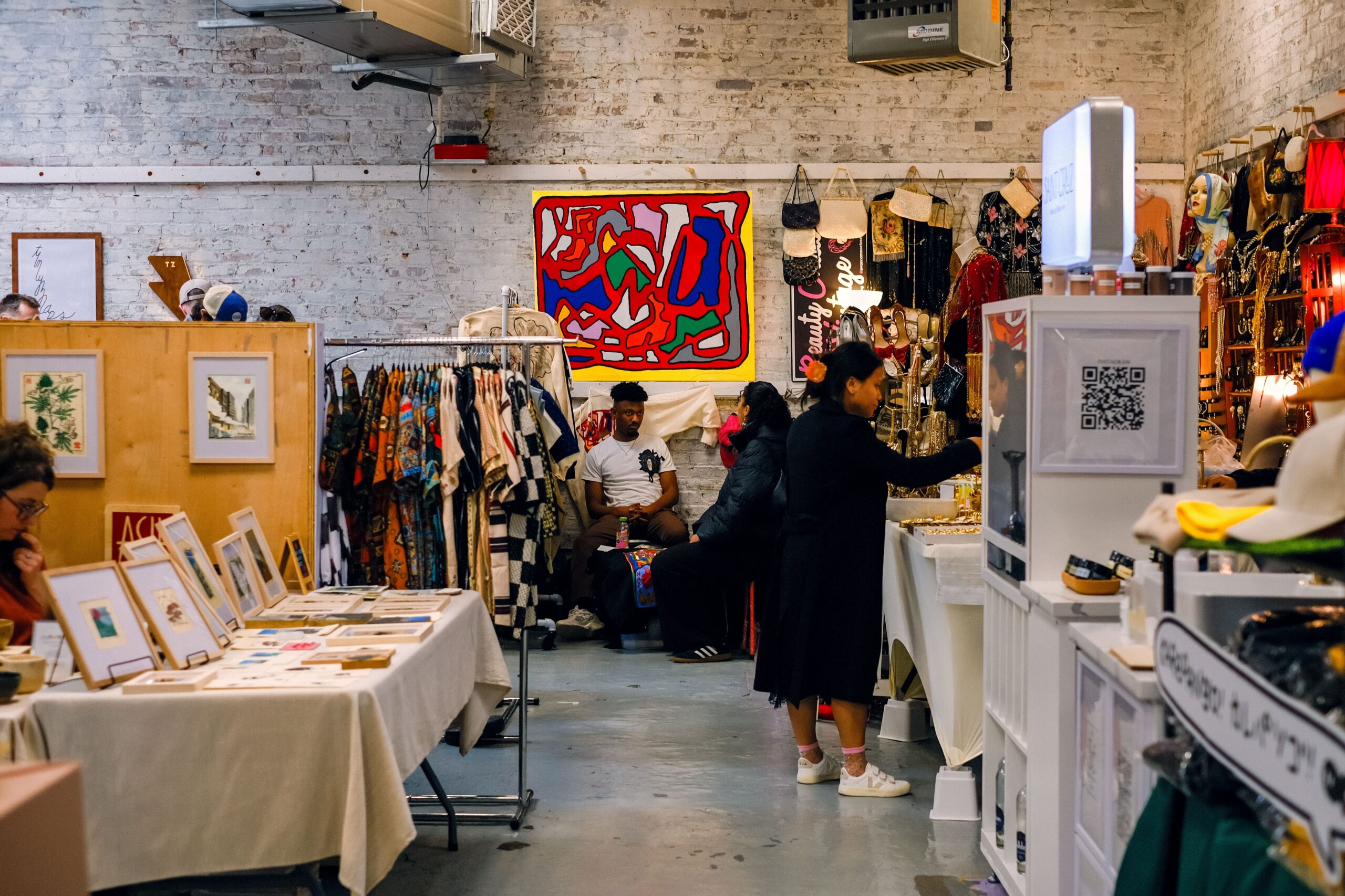 A bustling flea market in NoMad with vendors selling vintage clothing, jewelry, artwork, and handmade goods inside a brick-walled indoor space.
