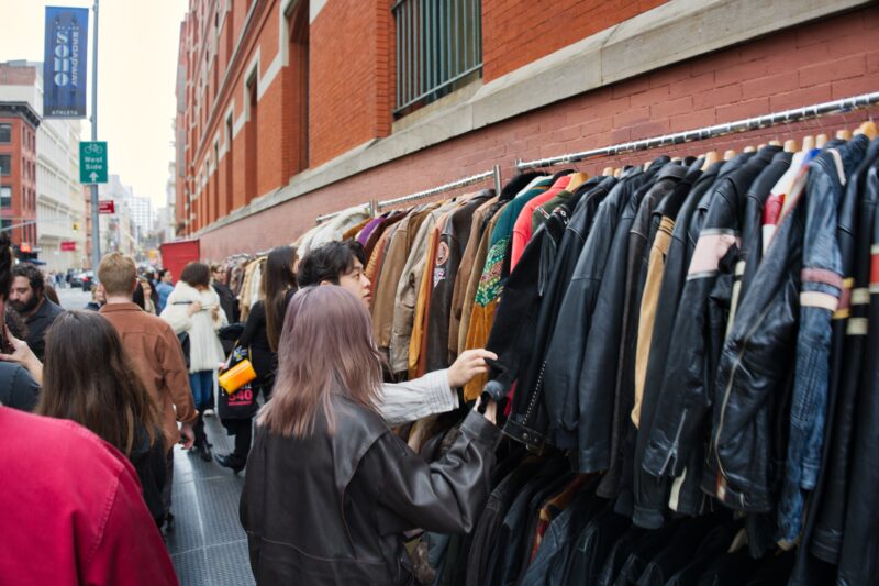 People browsing vintage leather jackets at an outdoor clothing market along SoHo Design District in New York City.