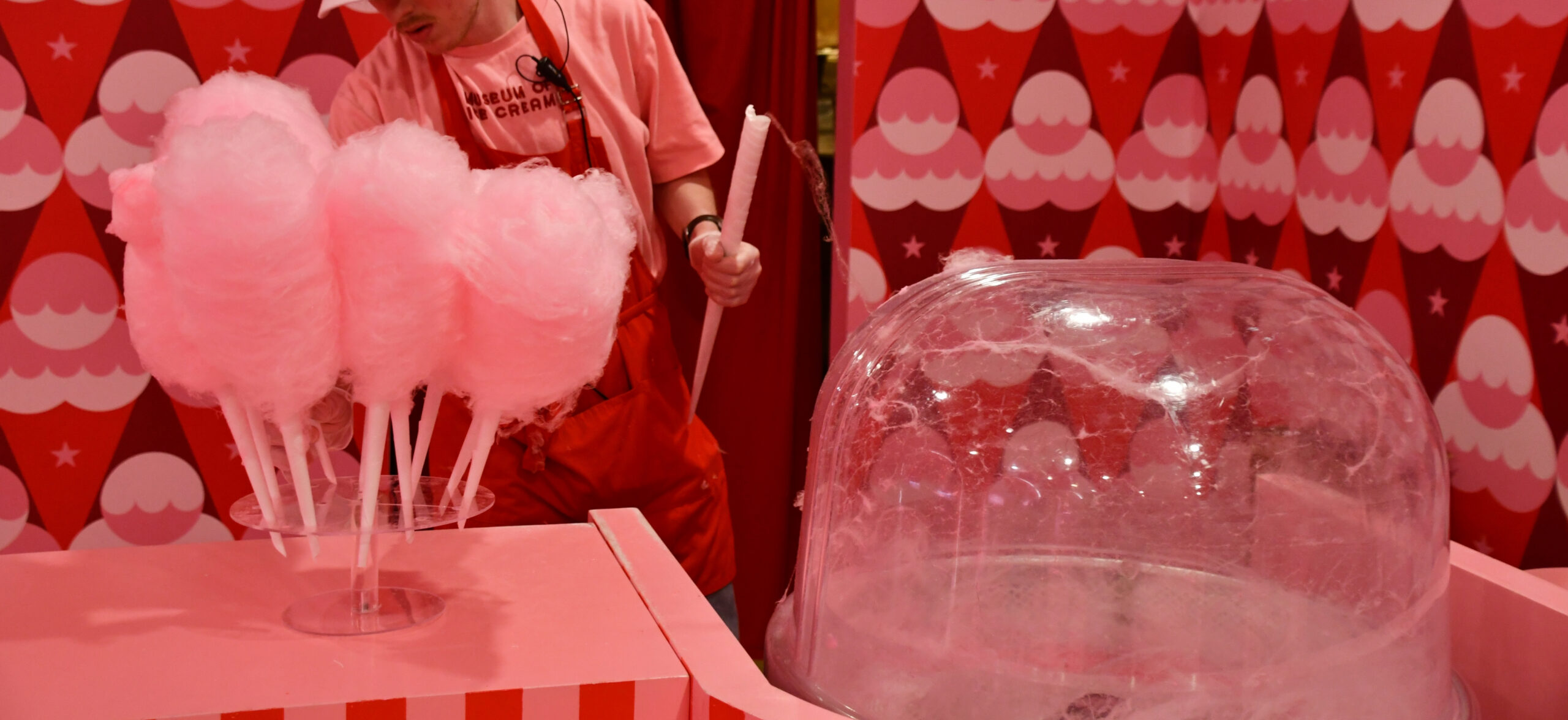 Staff member making pink cotton candy at the Museum of Ice Cream in New York City, surrounded by colorful ice cream-themed decor.