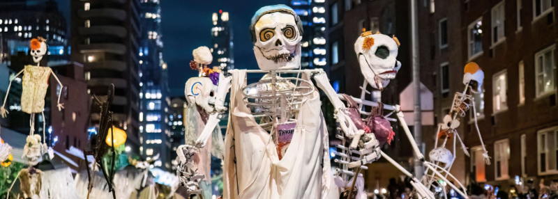 Giant skeleton puppets tower over crowds of costumed spectators during New York City’s Village Halloween Parade at night.