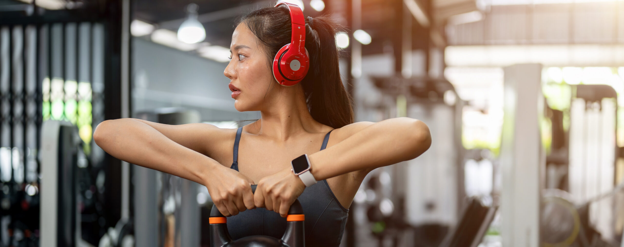 A woman working out solo in a modern gym while holding a kettlebell and wearing headphones, highlighting individual fitness training in Washington, DC.