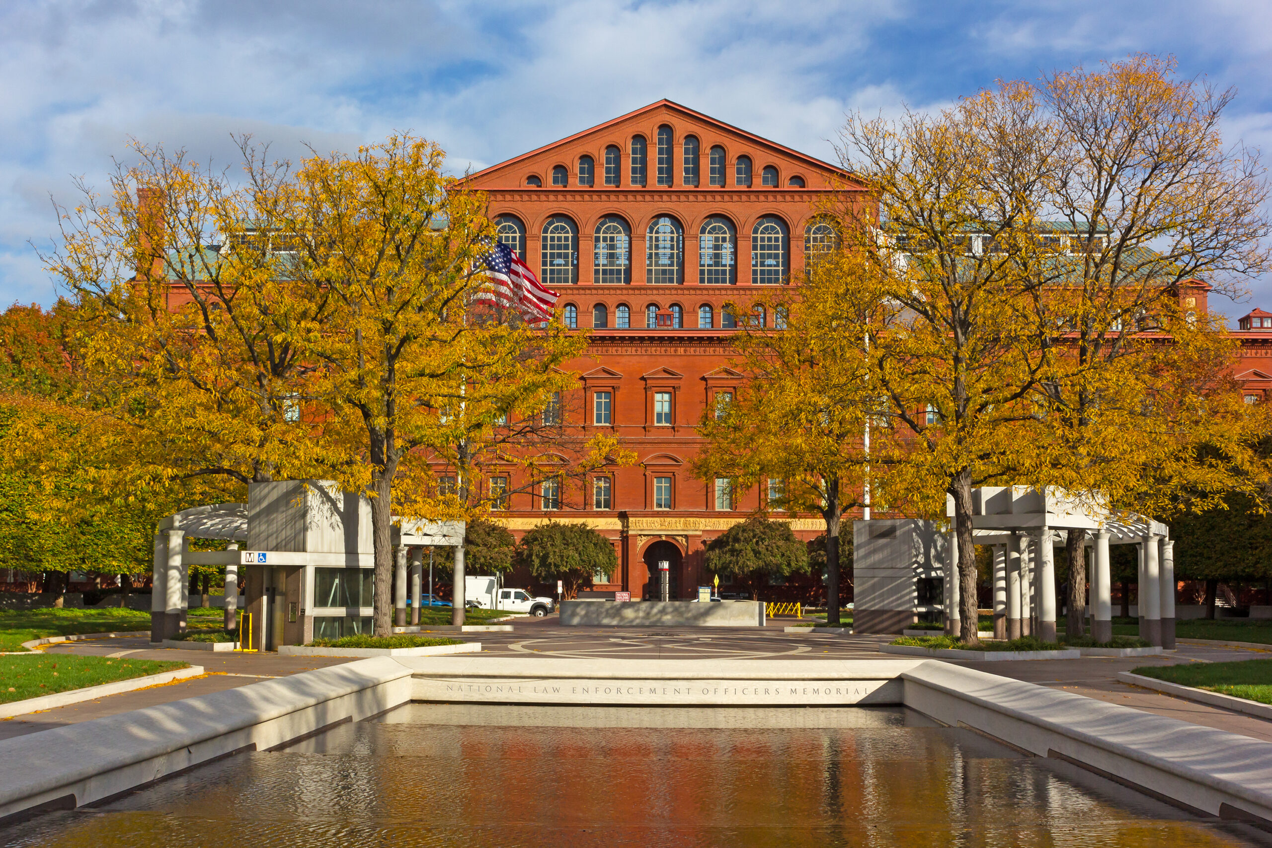 National Law Enforcement Officers Memorial reflecting pool in Judiciary Square, with the red-brick National Building Museum behind golden autumn trees.