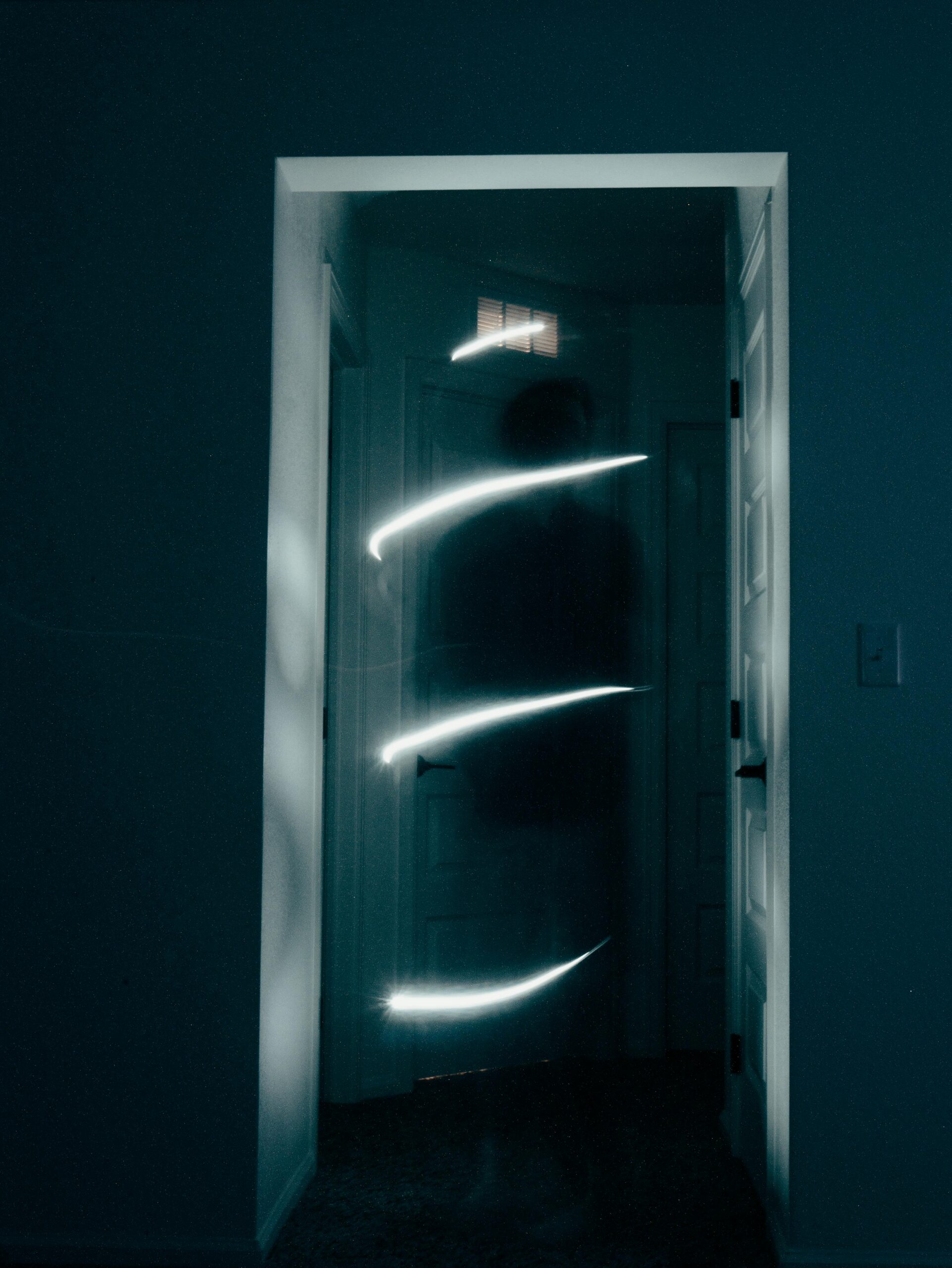 A dimly lit doorway with a faint human figure and a spiral trail of light in the center, suggesting movement or a long exposure effect.