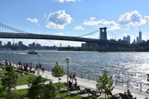 Williamsburg waterfront park with the Williamsburg Bridge, East River, and Lower Manhattan skyline on a sunny summer afternoon in Brooklyn, NYC.