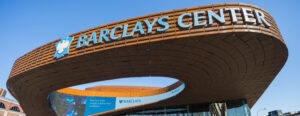 Exterior view of Barclays Center in Brooklyn, New York, featuring the arena’s iconic curved architecture and large entrance plaza on a clear sunny day.