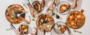 Table filled with wood-fired pizzas topped with fresh mozzarella, basil, and cured meats, representing the best food in Brooklyn.