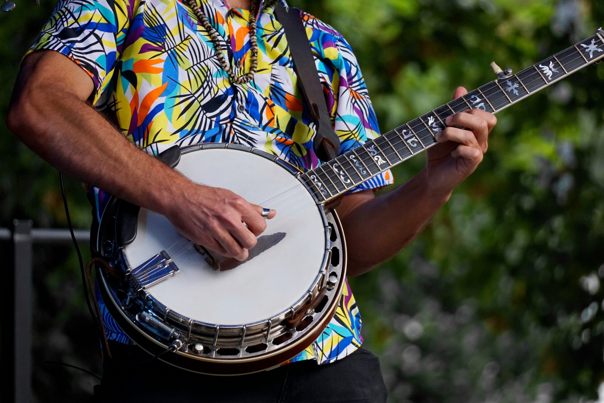 Close-up of a musician playing a banjo outdoors, wearing a colorful patterned shirt at a Brooklyn Americana music festival.