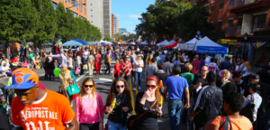 A crowded Atlantic Antic street festival in Brooklyn, with thousands of people walking between food stalls and vendor tents along the closed-off avenue.