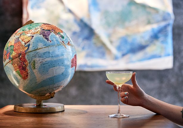 Globe on a table next to someone holding a cocktail