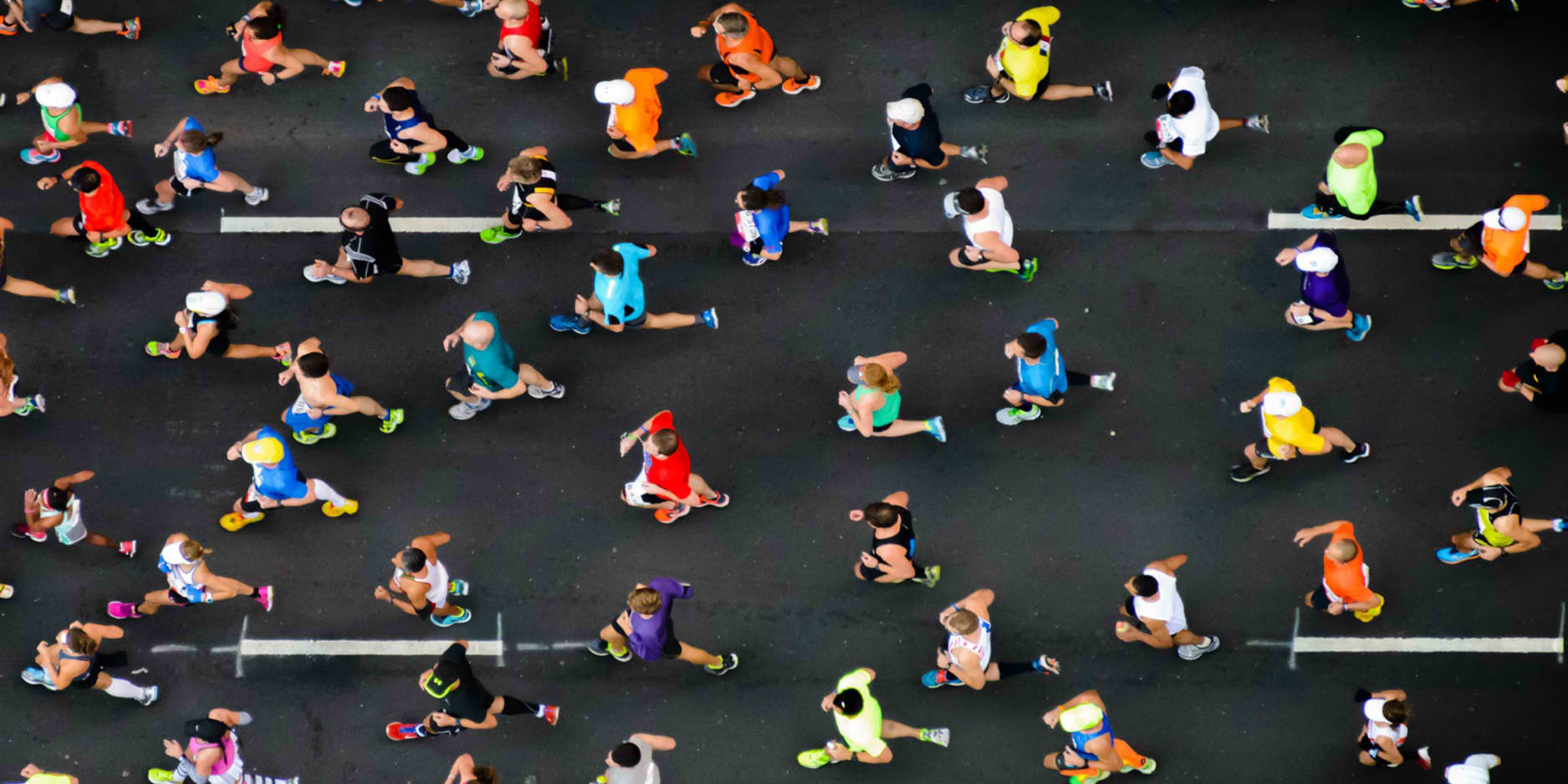 Aerial view of a large group of runners on a road during a marathon. The runners are wearing various brightly colored athletic clothing.