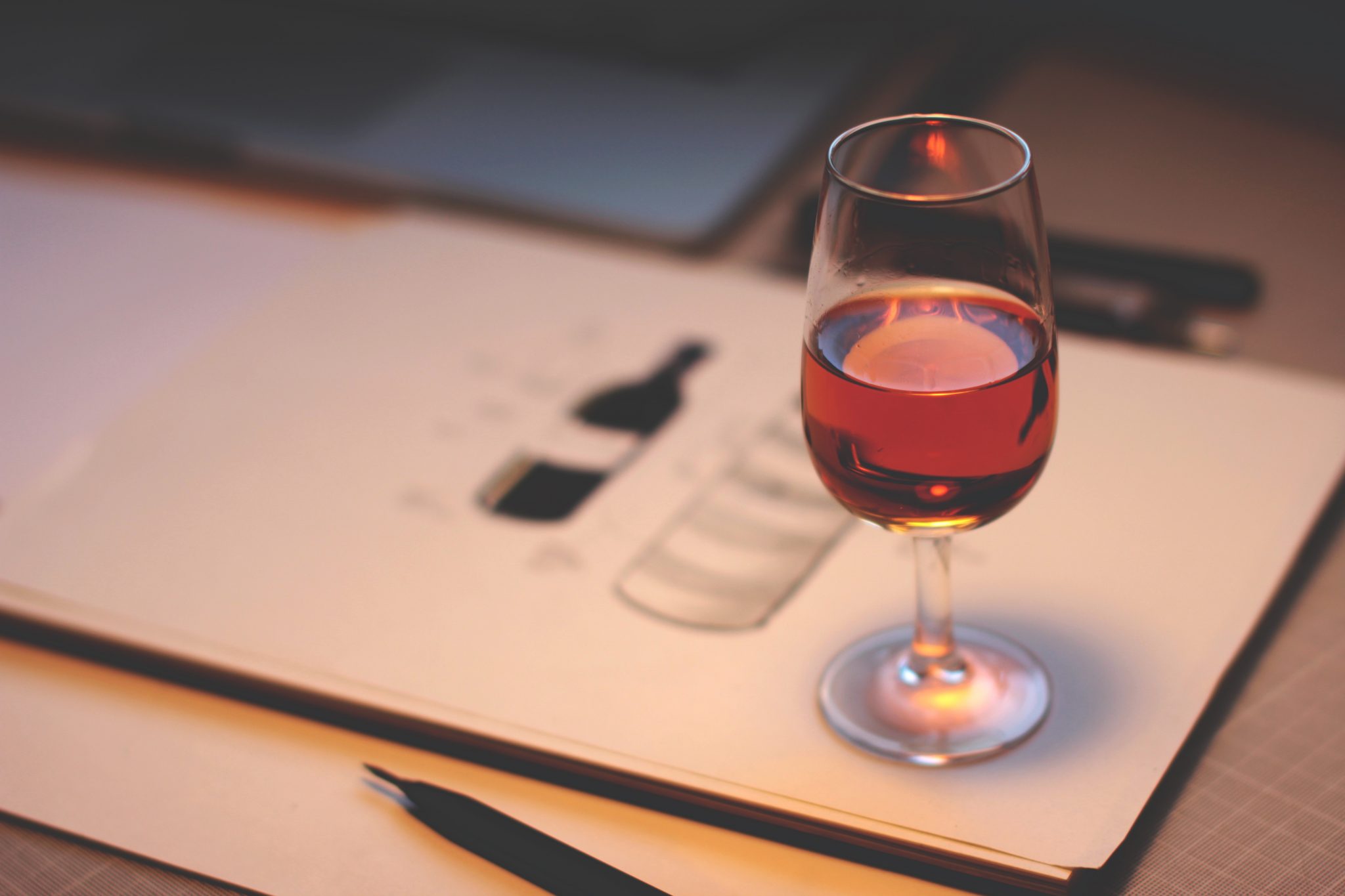 Wine glass on desk with pen and paper describing wines