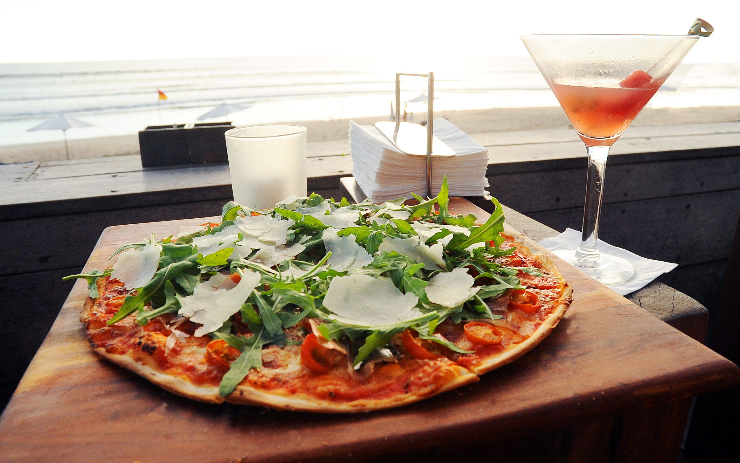 arugula shaved parmesan on flat styled margherita pizza with view of the beach ahead