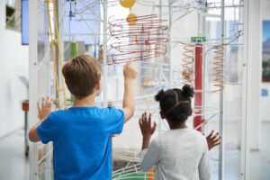 two kids in a museum looking at a colorful swirly contraption