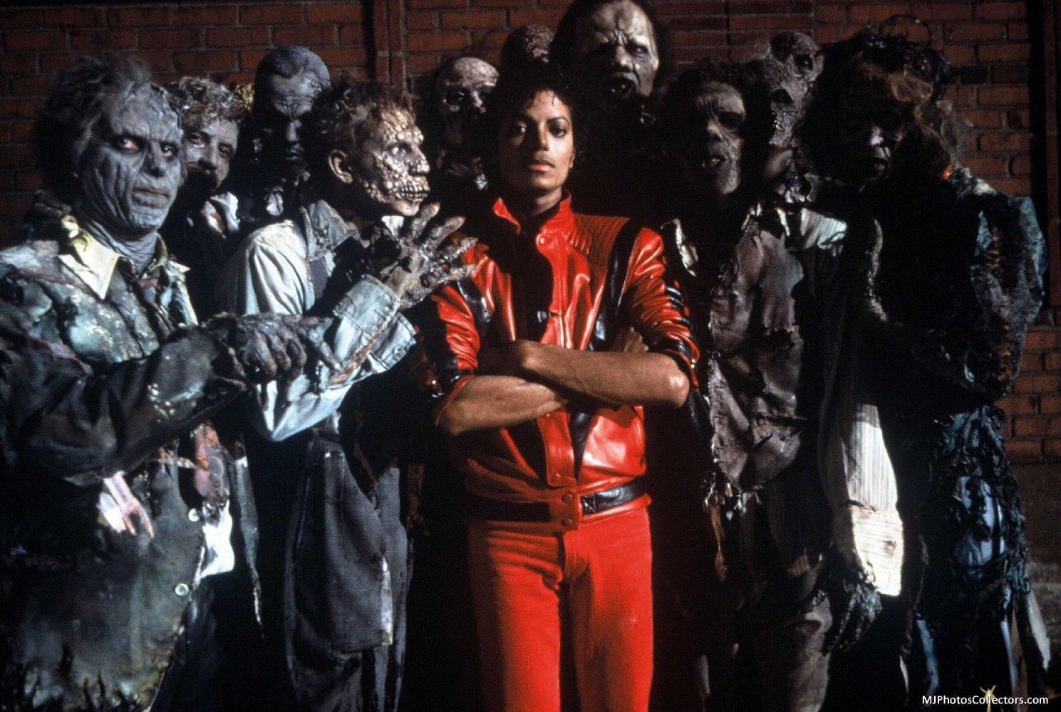 A person in a bright red outfit stands confidently with arms crossed, surrounded by a group of people in tattered costumes with makeup resembling zombies.