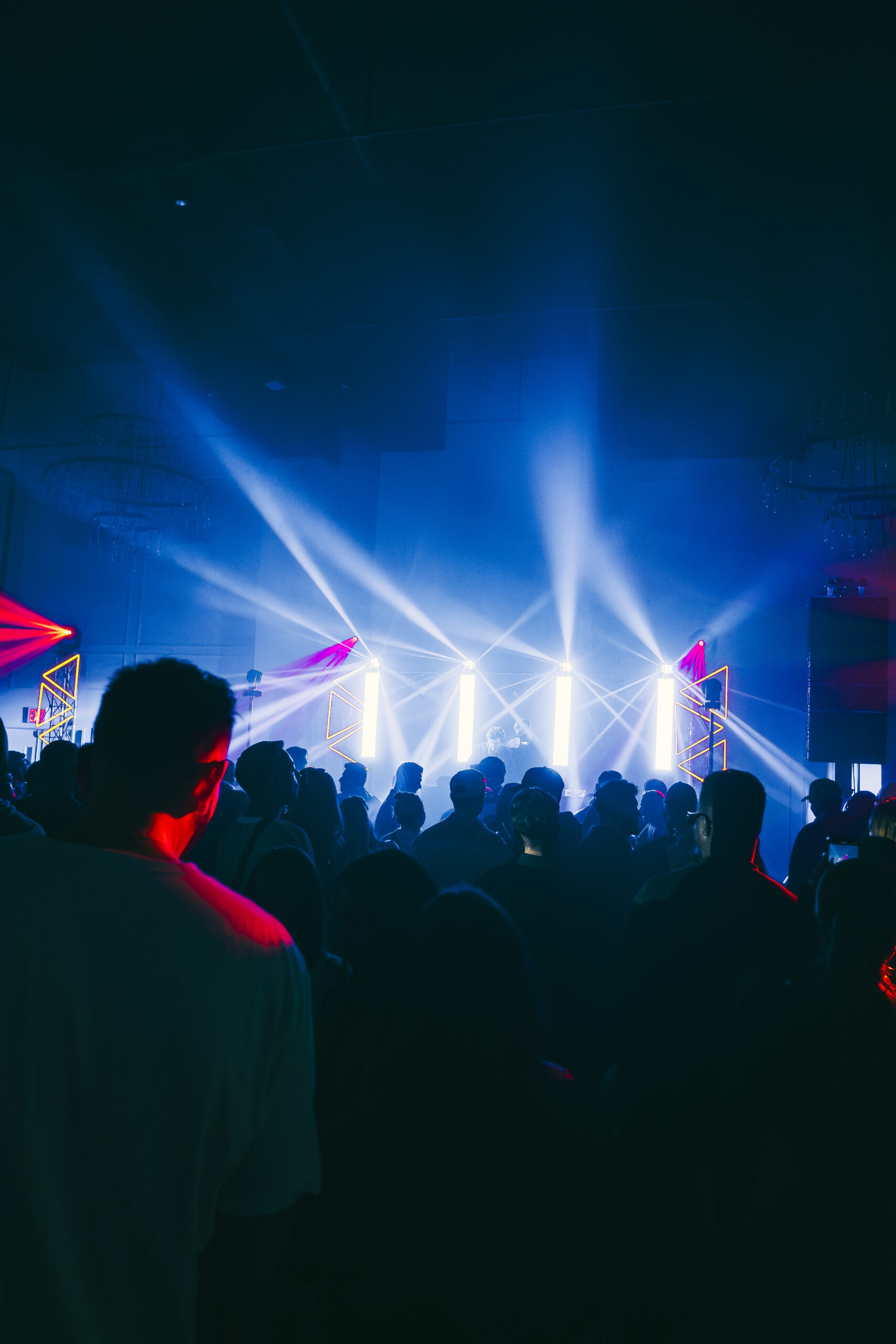 A crowd enjoys a concert in a dimly lit venue with bright blue and white stage lights.