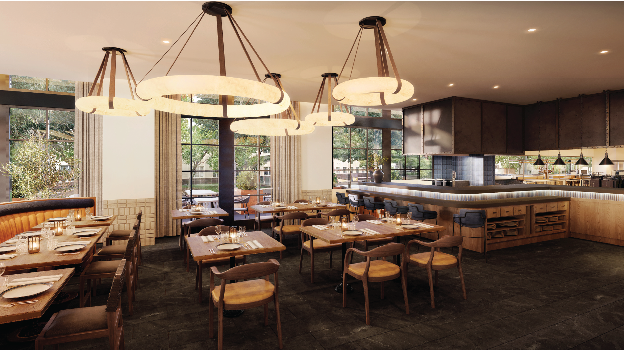 A modern restaurant interior with wooden tables and chairs, large circular light fixtures, and an open kitchen. Large windows provide natural light and a view of trees outside.