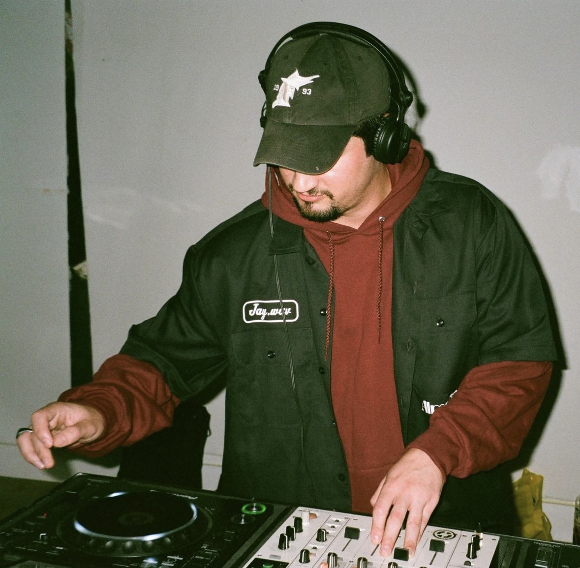 Person wearing headphones and a cap is DJing with audio equipment.