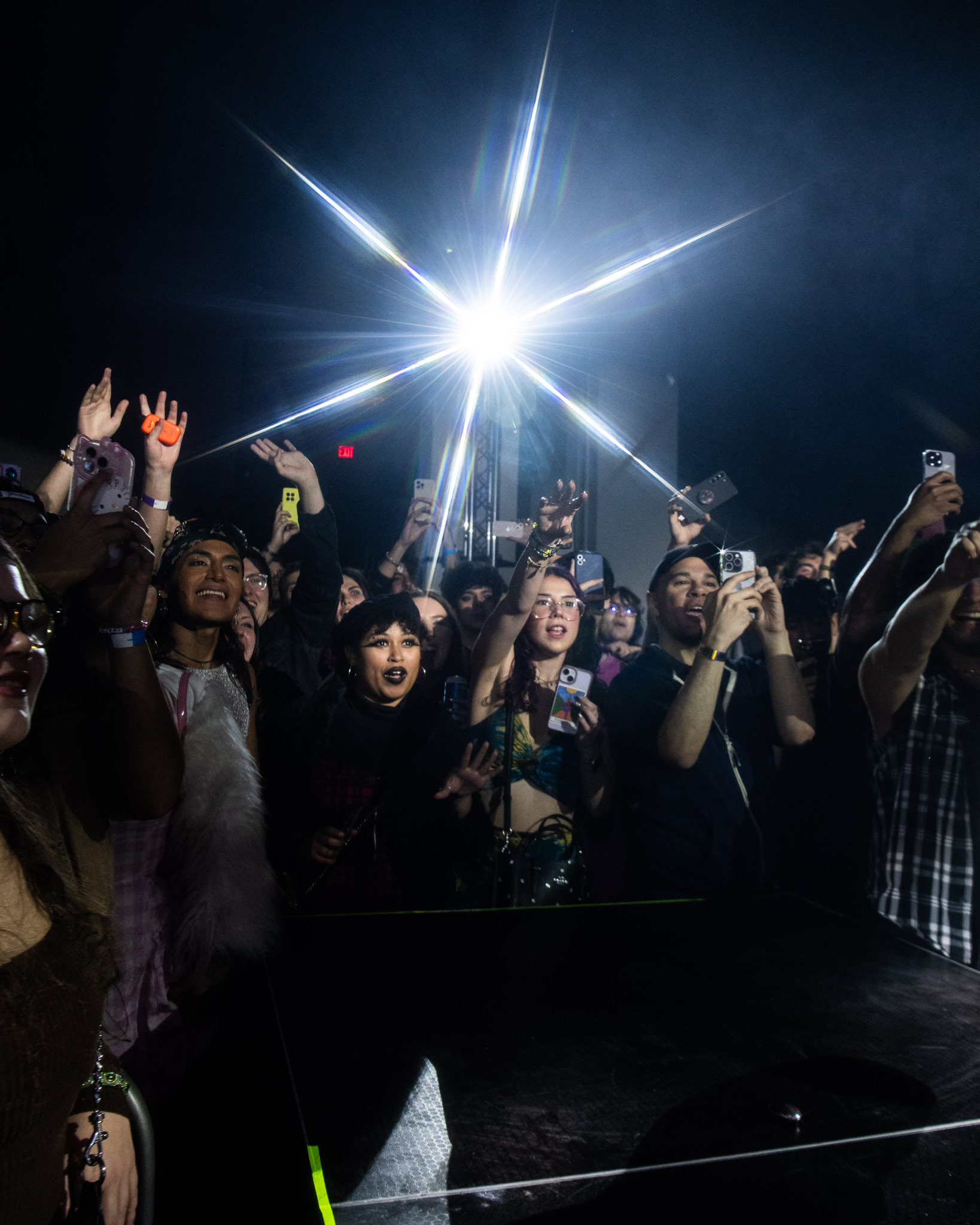 A crowd at a concert holds up their phones, facing a bright spotlight.