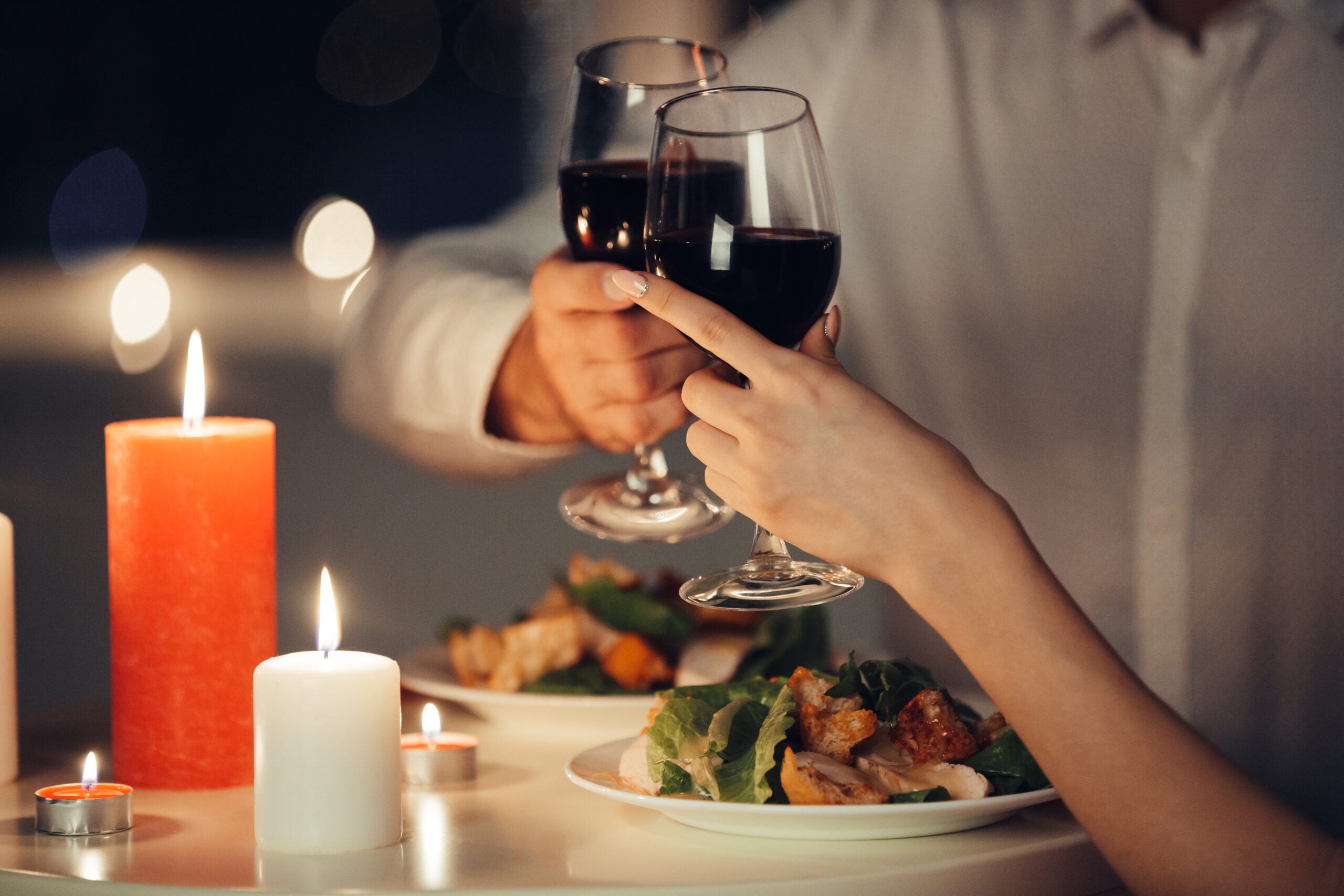 Two people clink glasses of red wine over a table set with salads and lit candles—one of the romantic Valentine's Day ideas in New York.