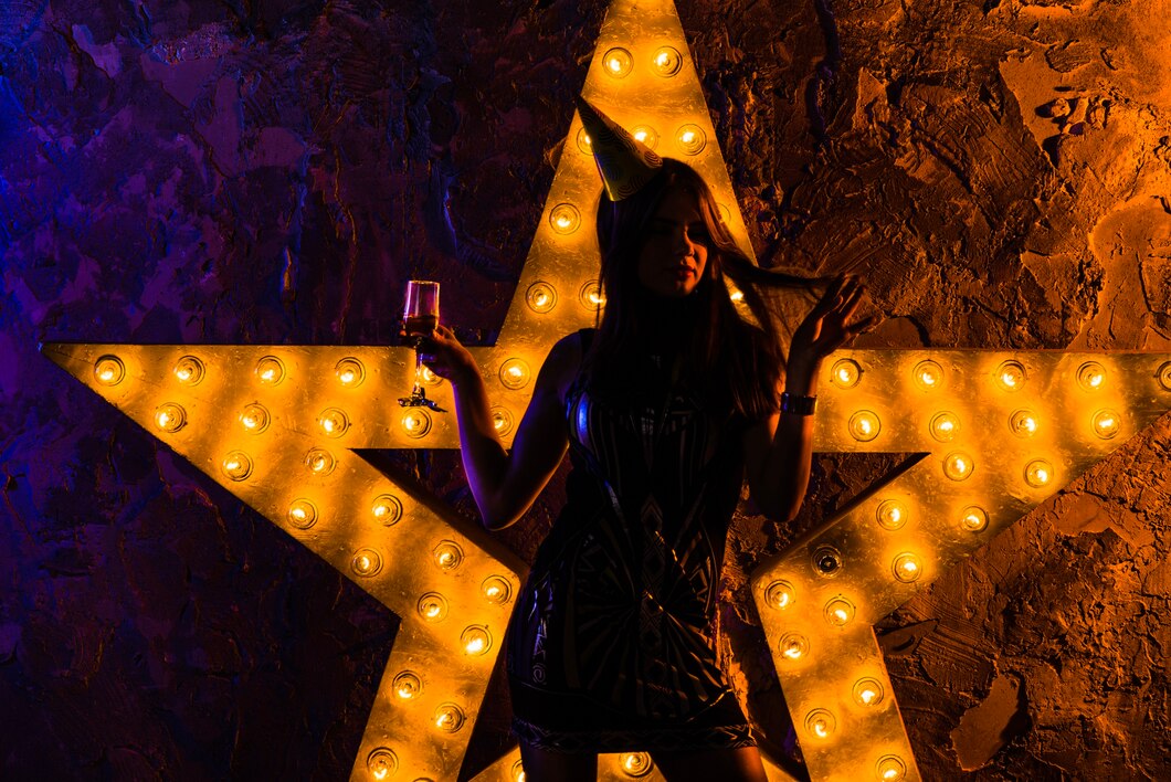 A person in a party hat holding a drink stands in front of a large illuminated star-shaped light fixture on a textured wall, evoking the vibrant energy of Broadway in Chicago.