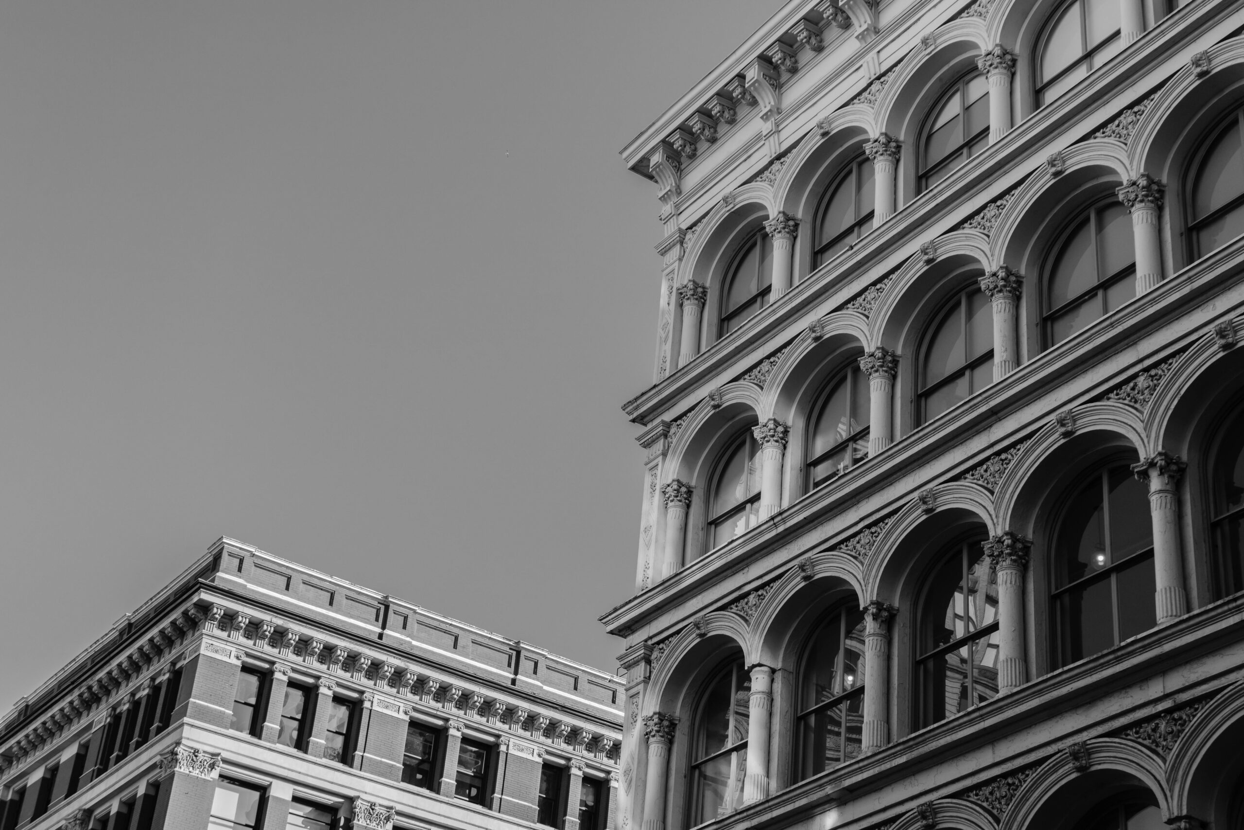 Two multi-story buildings with arched windows and decorative architectural details, shown in black and white against a clear sky, capture the timeless elegance of NYC architecture.