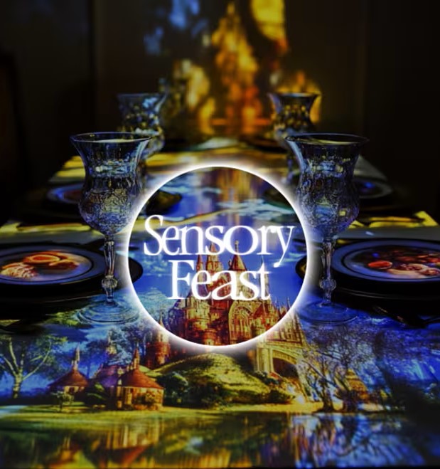A dining table with elegant glassware and plates, overlaid with vivid projected images of a castle and landscape, features the text "Sensory Feast" in the center.