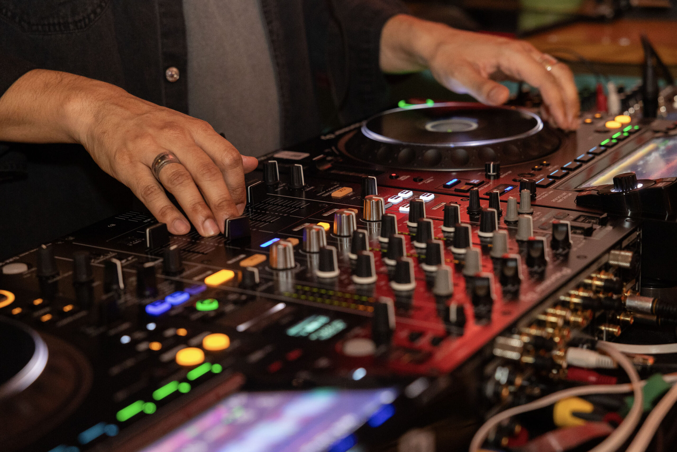 Close-up of a person's hands adjusting controls on a professional DJ mixer and turntable during a live music performance.