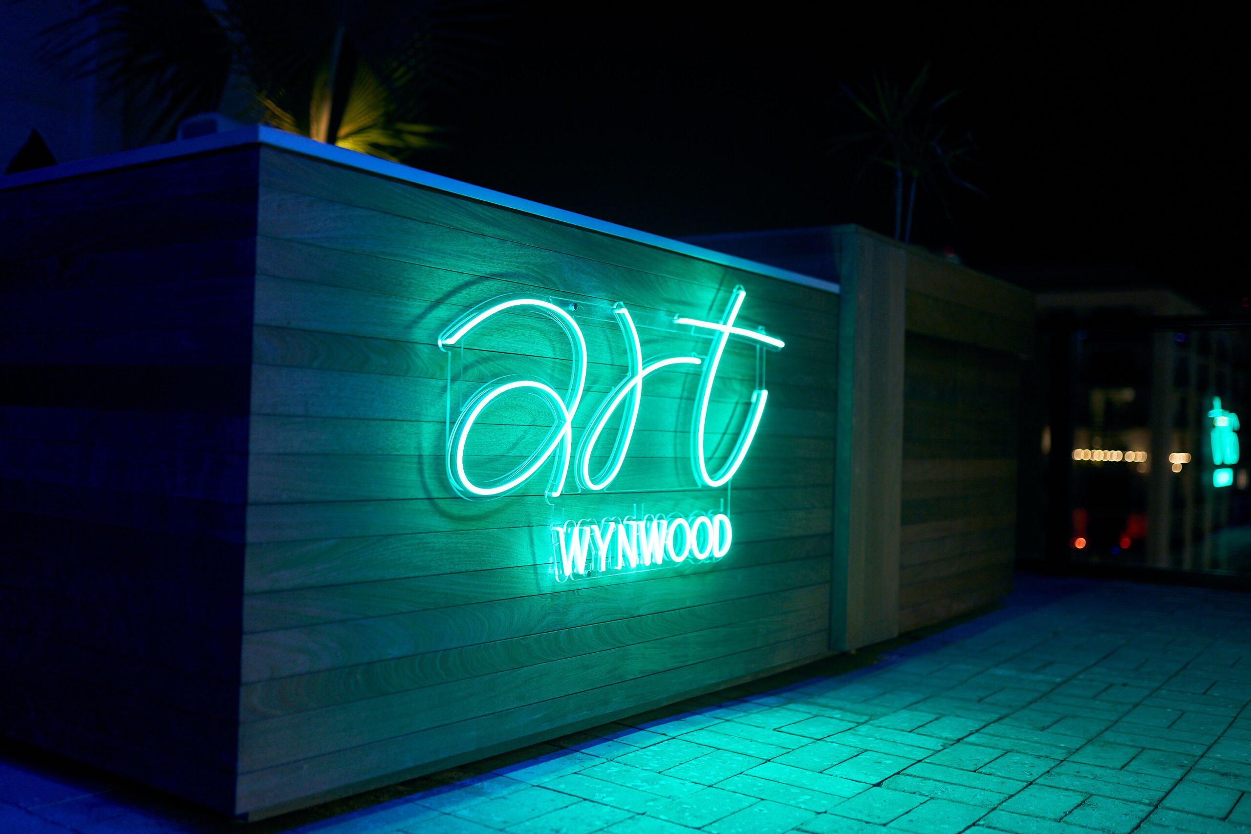 A neon sign reading "art WYNWOOD" is mounted on a wooden wall outdoors at night.