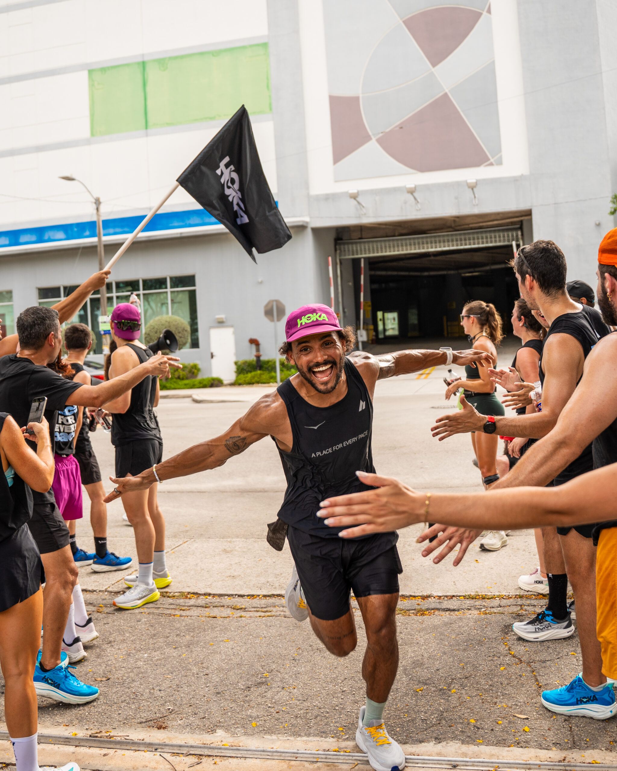 A smiling runner in athletic gear high-fives people lined up on both sides of a street, with one person holding a flag in the background.