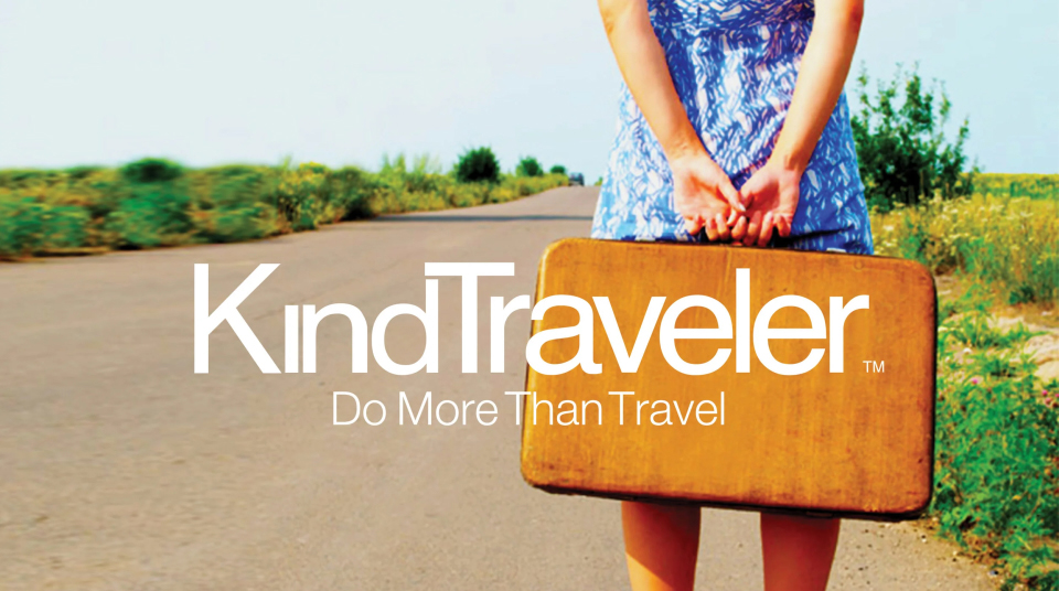 Person in a blue dress stands on a rural road holding a vintage suitcase, with "KindTraveler Do More Than Travel" text overlayed on the image.