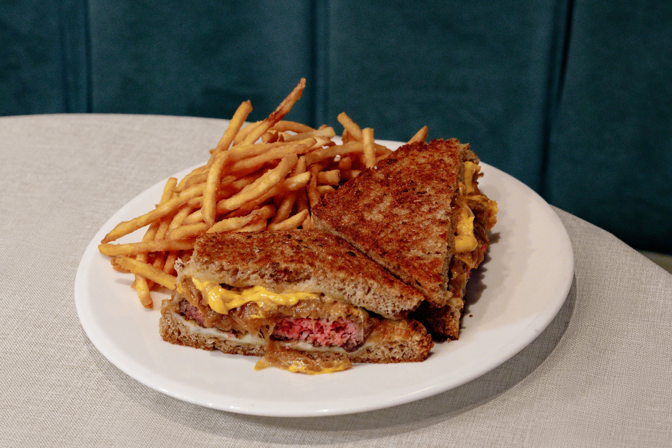 A plate of French fries and a grilled cheese sandwich with visible beef patty and melted cheese, served on a white plate on a table.