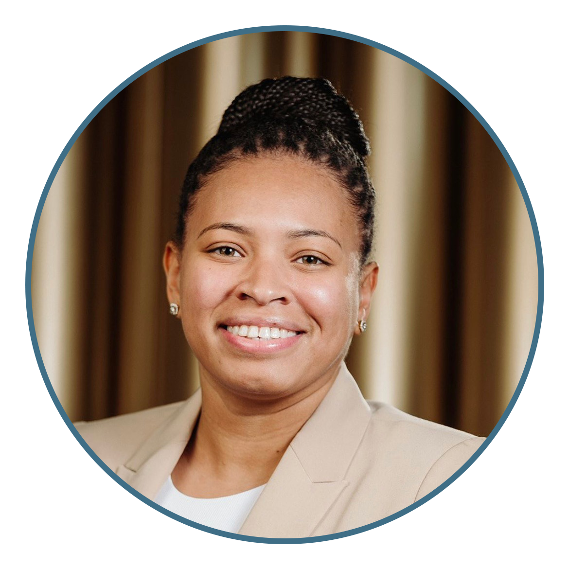 A woman with braided hair in a bun, wearing a beige blazer and white top, smiles at the camera with a blurred background.