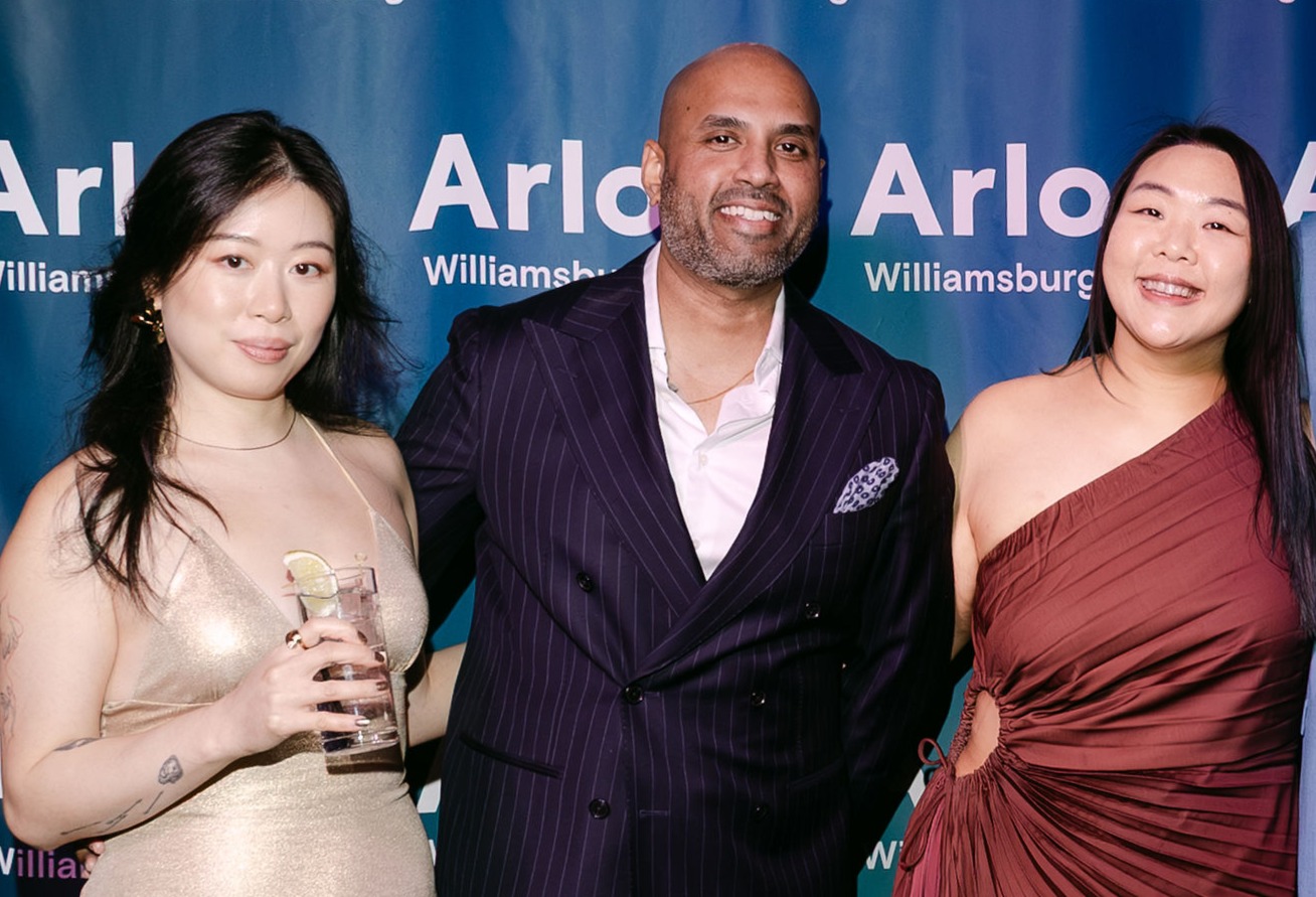 Three people pose together at an event in front of a blue step-and-repeat backdrop with "Arlo Williamsburg" written on it.