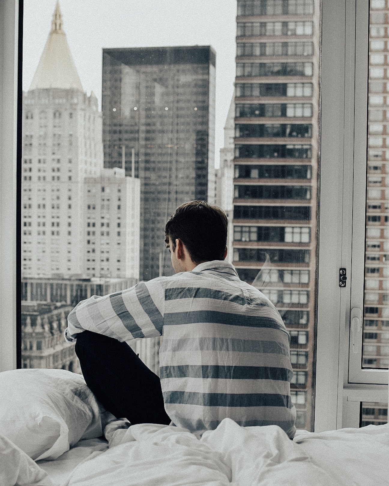 Man sitting on a bed looking out a window