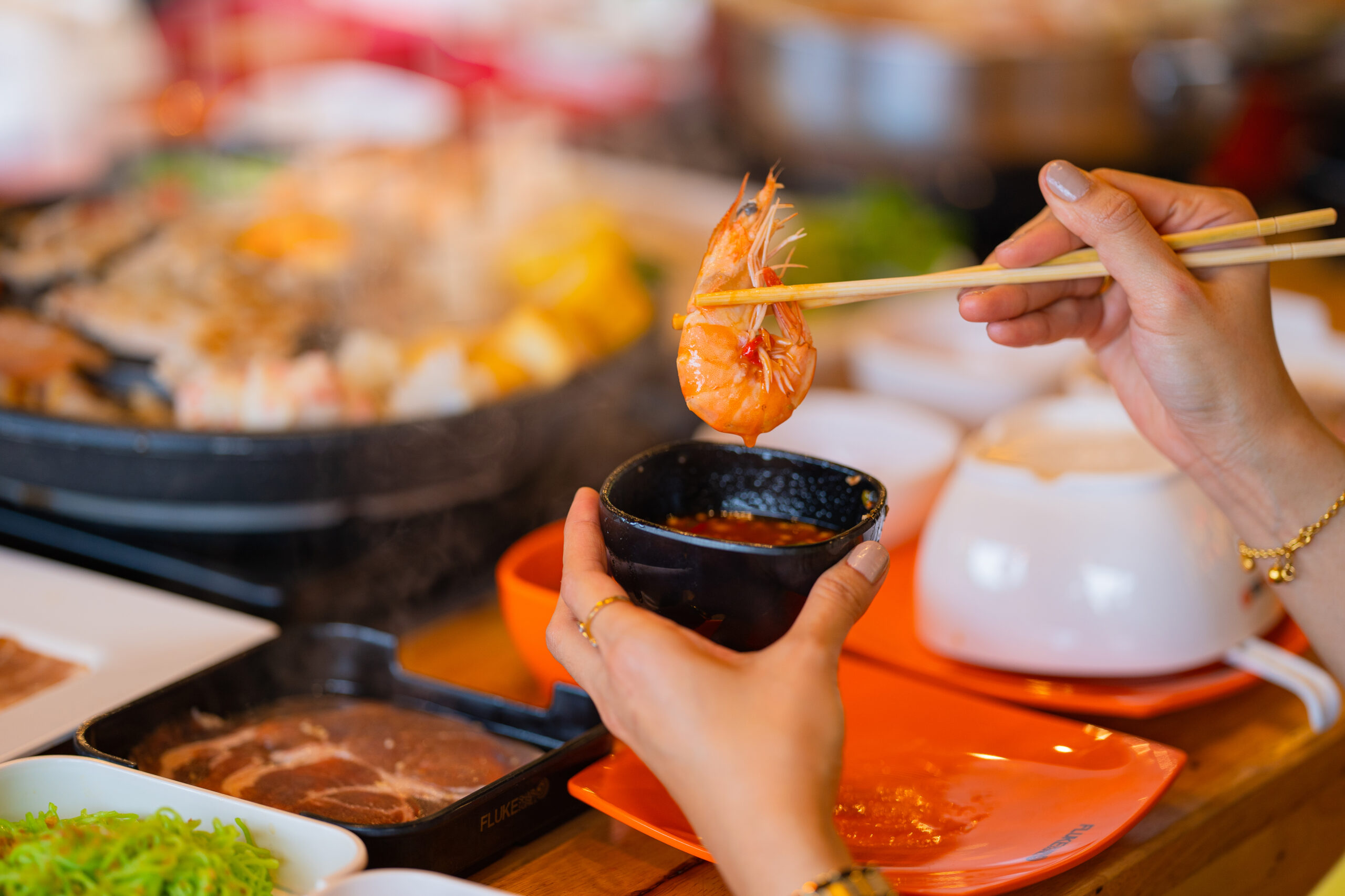 Close-up of a diner dipping a shrimp into a bowl of sauce with chopsticks at the 1-800-Lucky restaurant.