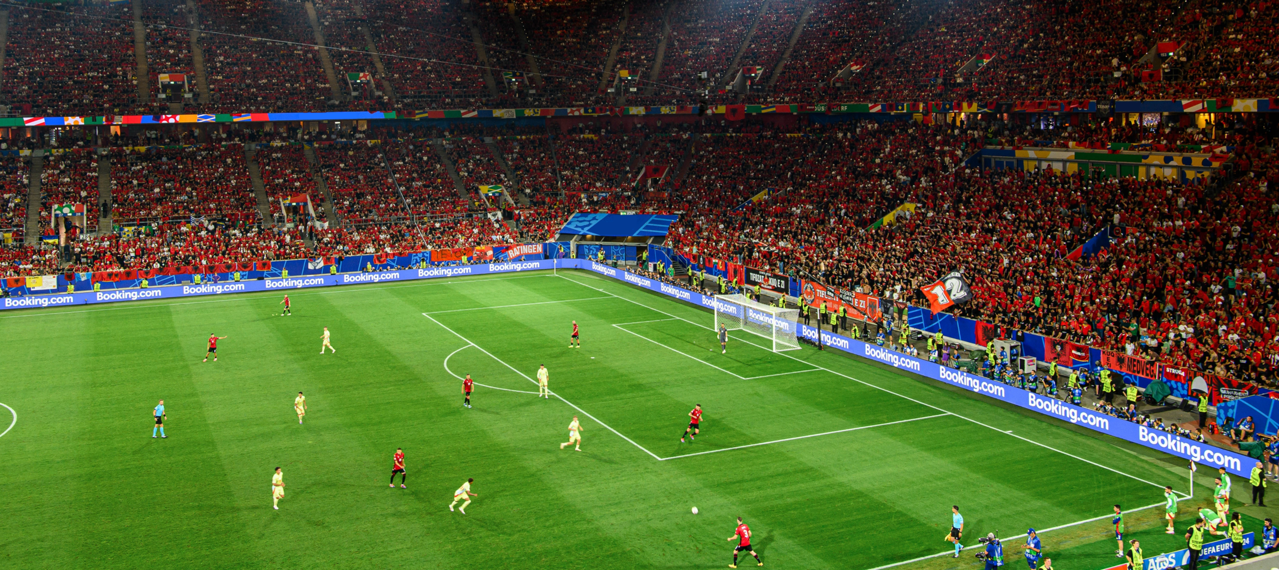 A wide-angle view of a packed soccer stadium at night during a match under bright lights.