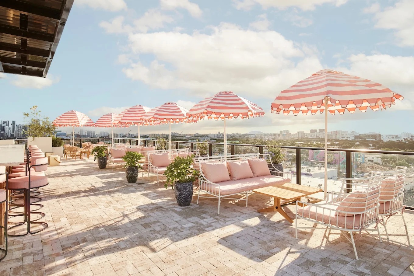 Rooftop lounge at Arlo Wynwood with pink seating, striped umbrellas, and skyline views.