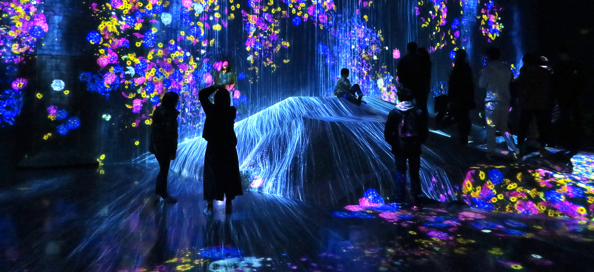 Visitors explore a vibrant immersive digital art installation at Superblue Miami, featuring colorful projections, interactive lights, and floor-to-ceiling visual displays.